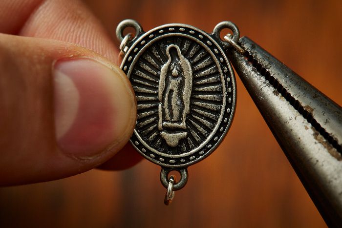 Demonstrating how to attach jump rings to the rosary's centrepiece